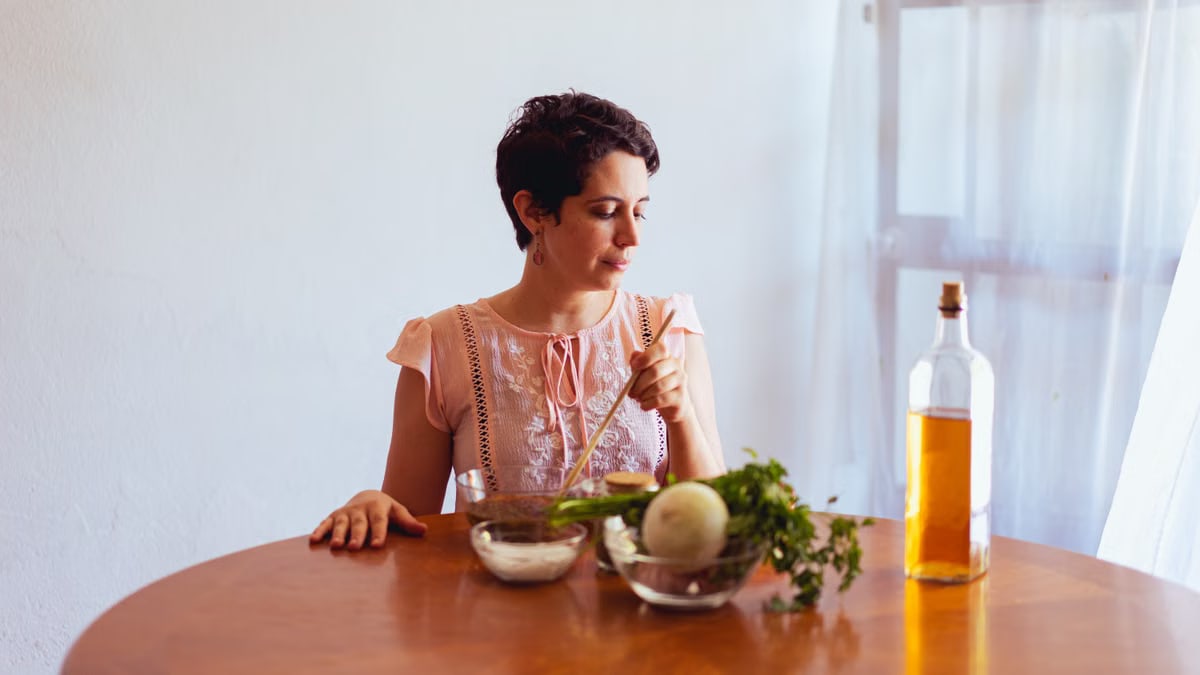 Woman in light dress preparing fresh ingredients with oil indoors.